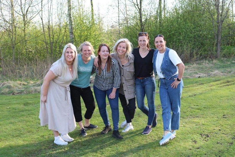 En grupp kvinnor som håller om varandra framför en skogsdunge