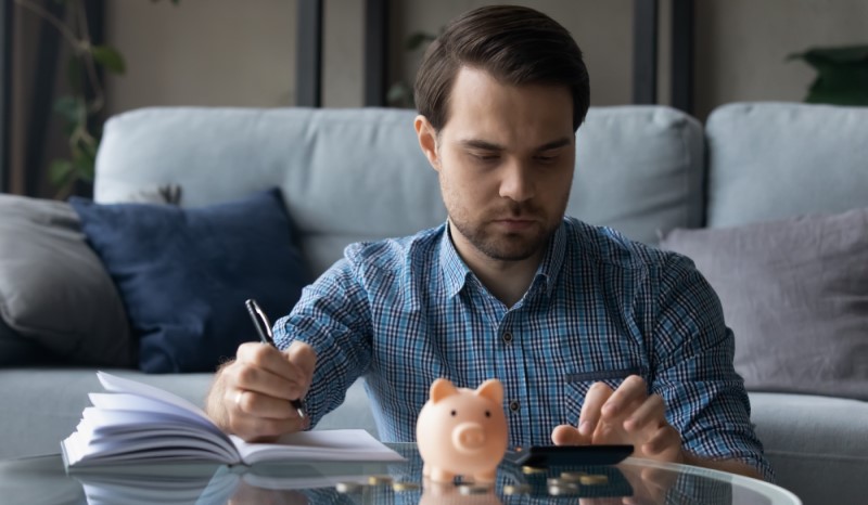 En man sitter vid ett bord med en miniräknare, en spargris och ett skrivblock framför sig.