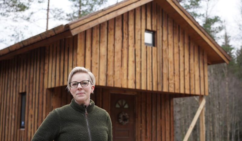 En kvinna står framför en timmerstuga.