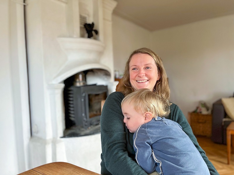 En kvinna med ett litet barn i famnen sitter framför en braskamin .