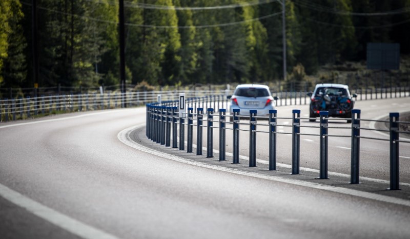 Motorväg med mitträcke. Till höger i bild syns en vit och en svart bil.