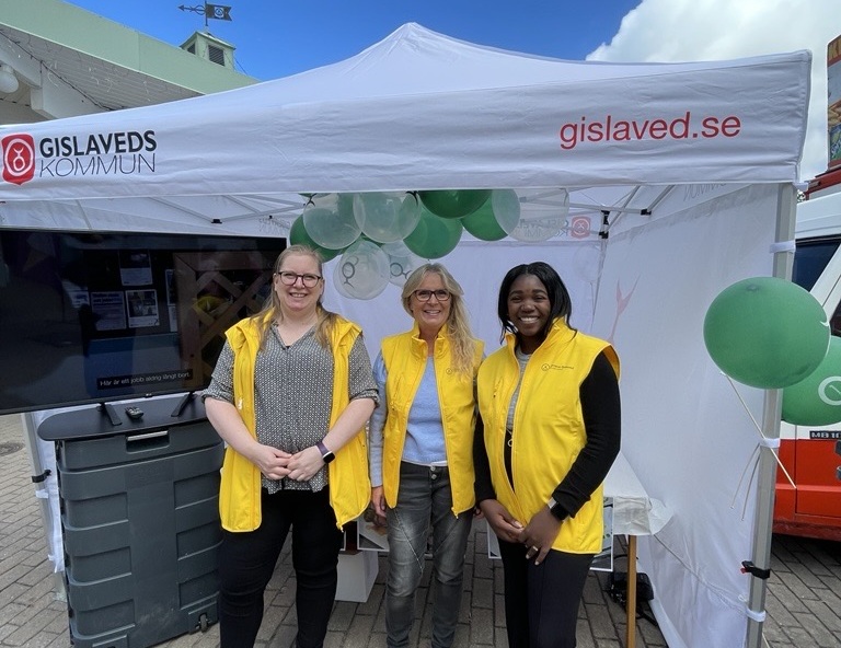 Ett utställningstält där tre medarbetare i citrongula västar står.