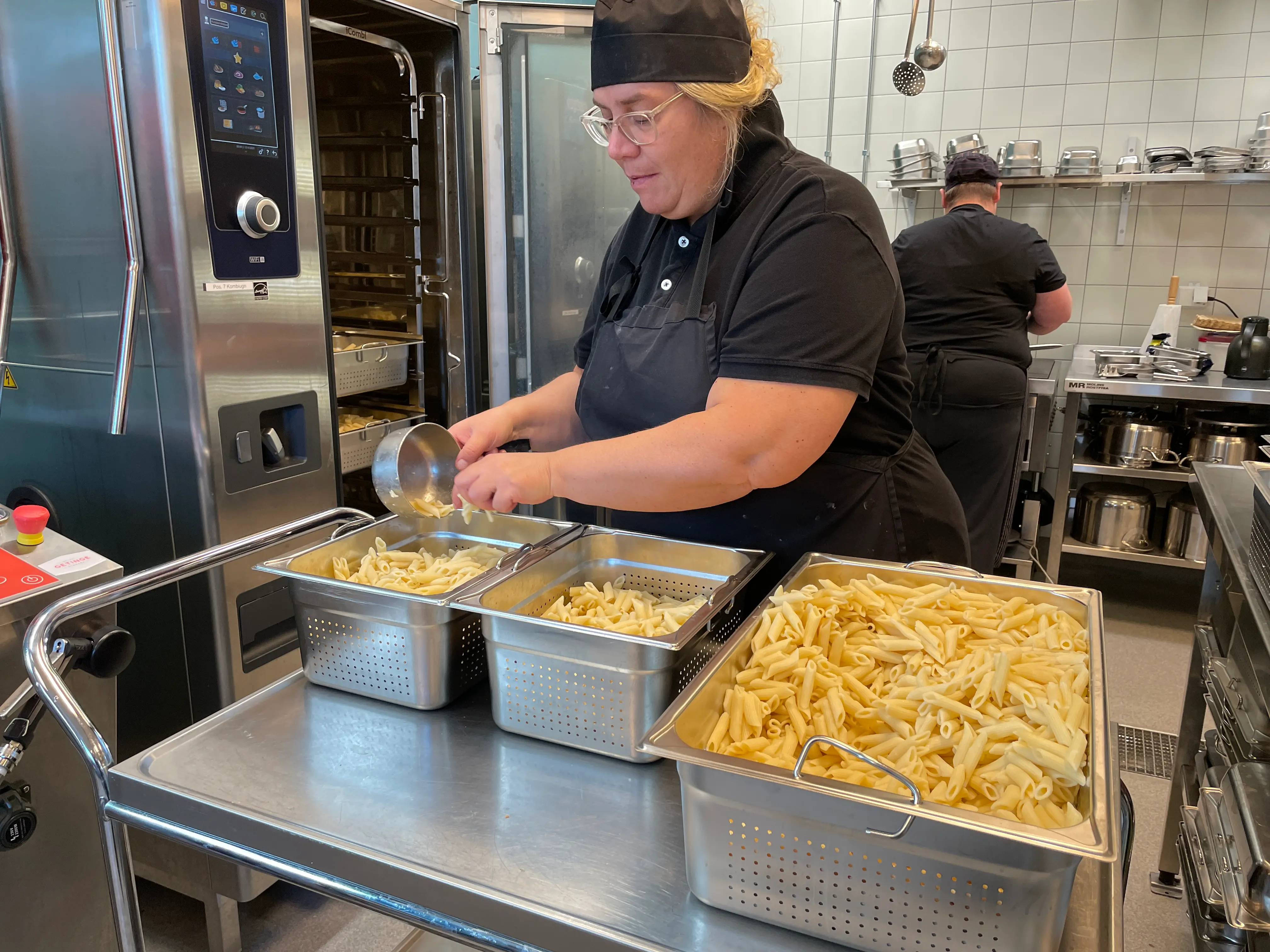 En kvinna som står i ett storkök och lagar mat.