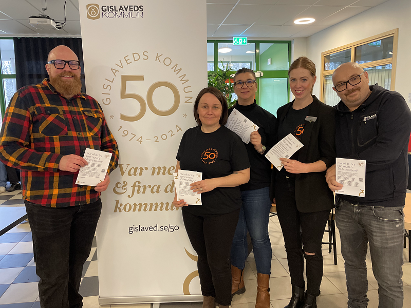 En grupp kvinnor och män framför en jubileumsskylt