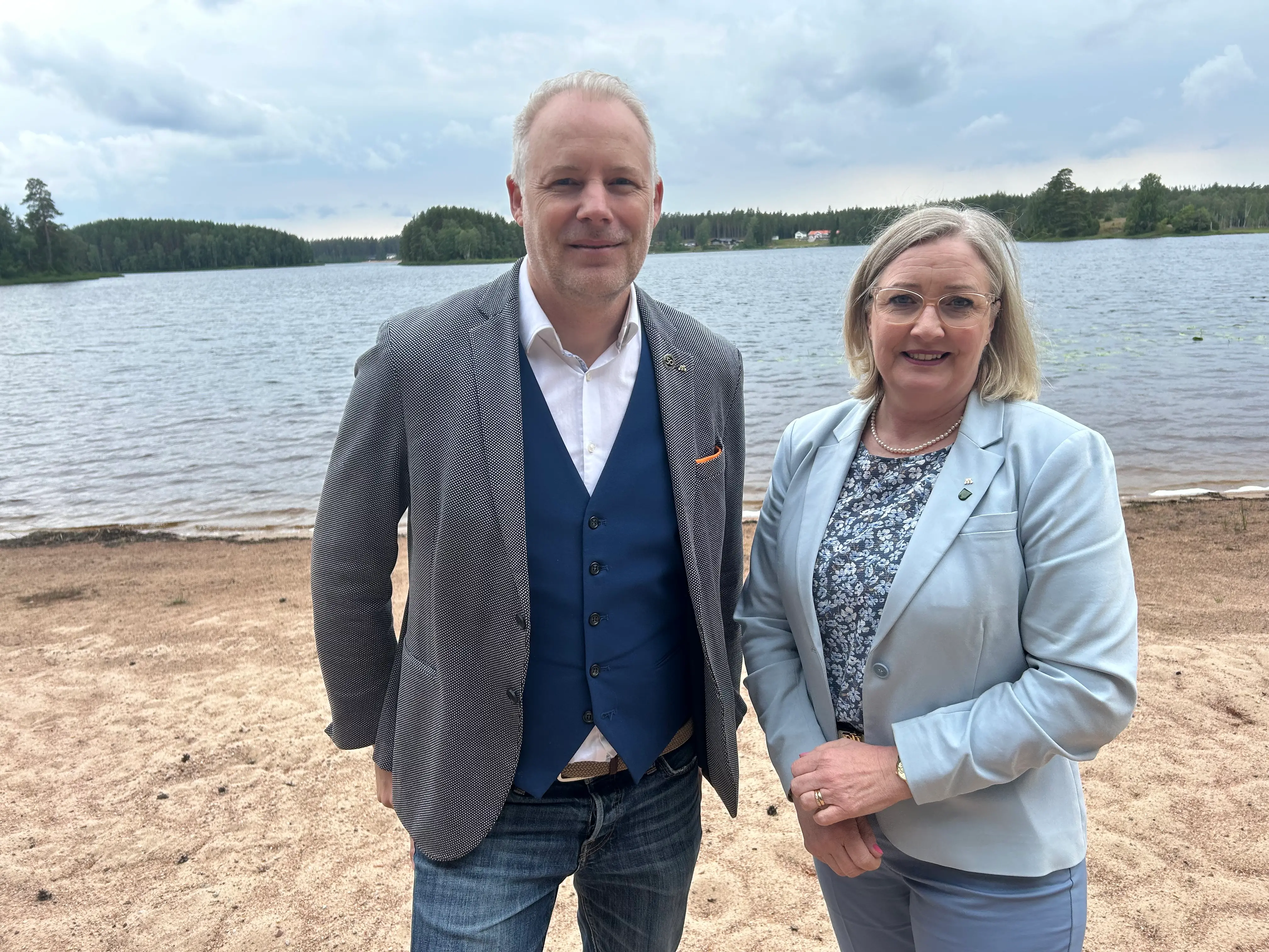 Anton Sjödell och Kristine Hästmark står vid en strand med en sjö i bakgrunden.