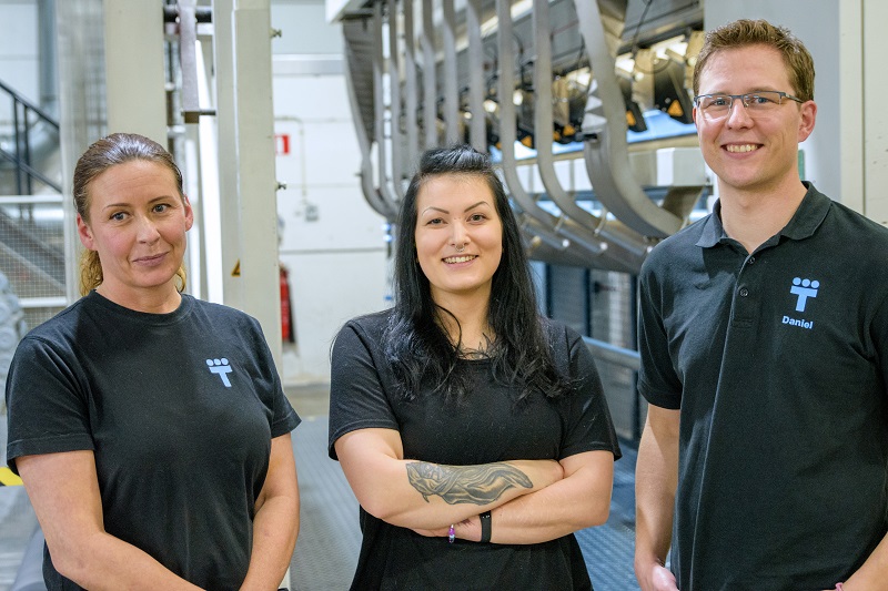 Tre personer står framför maskiner i en tillverkningshall