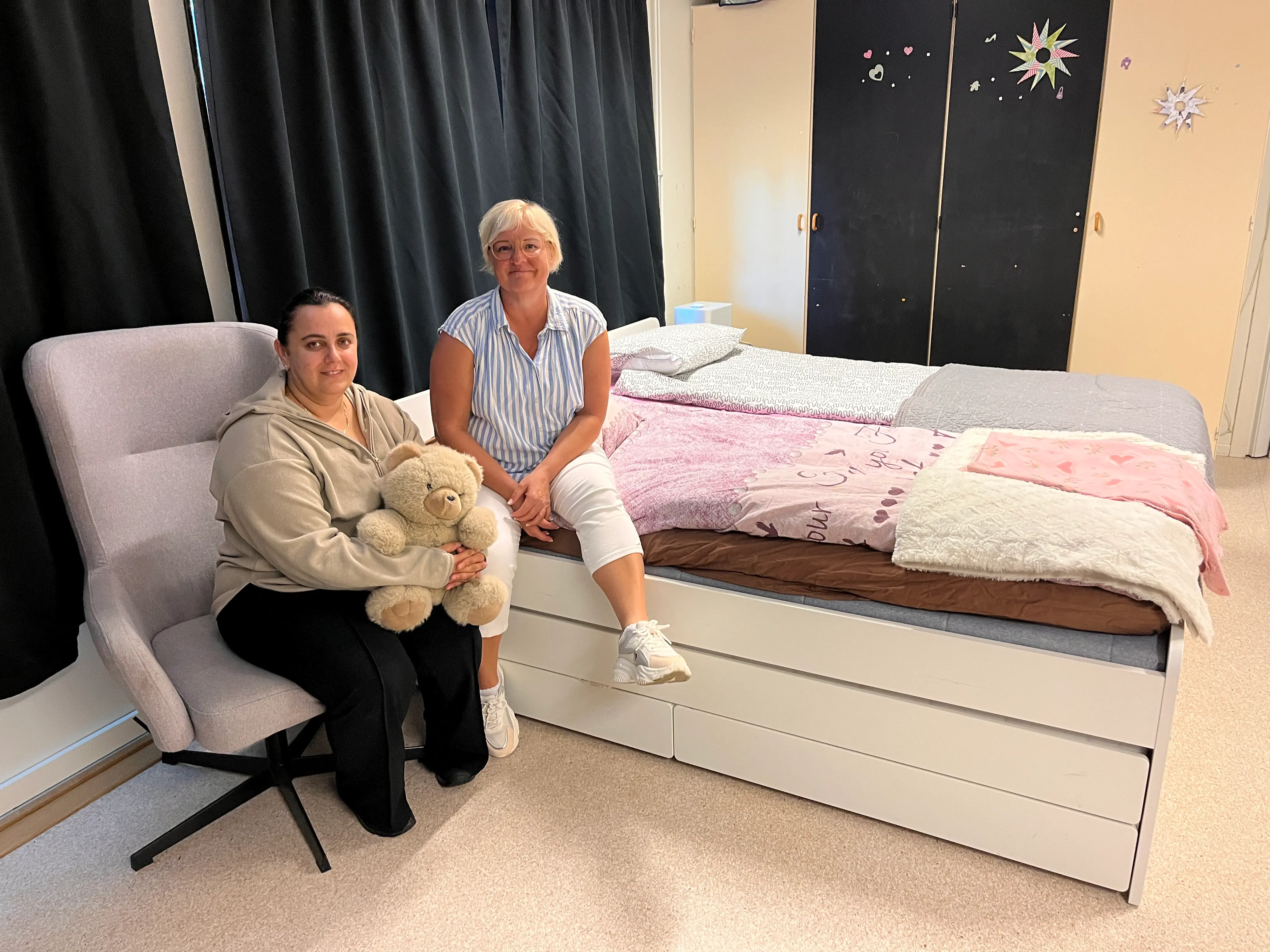 Foto på två kvinnor framföre en dubbelsäng.