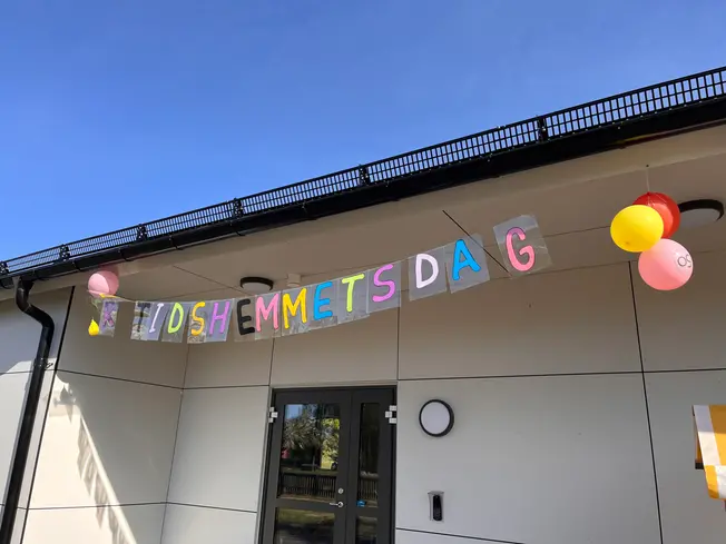 Ett foto på byggnaden med en skylt utanför dörren där det står "fritidshemmets dag".