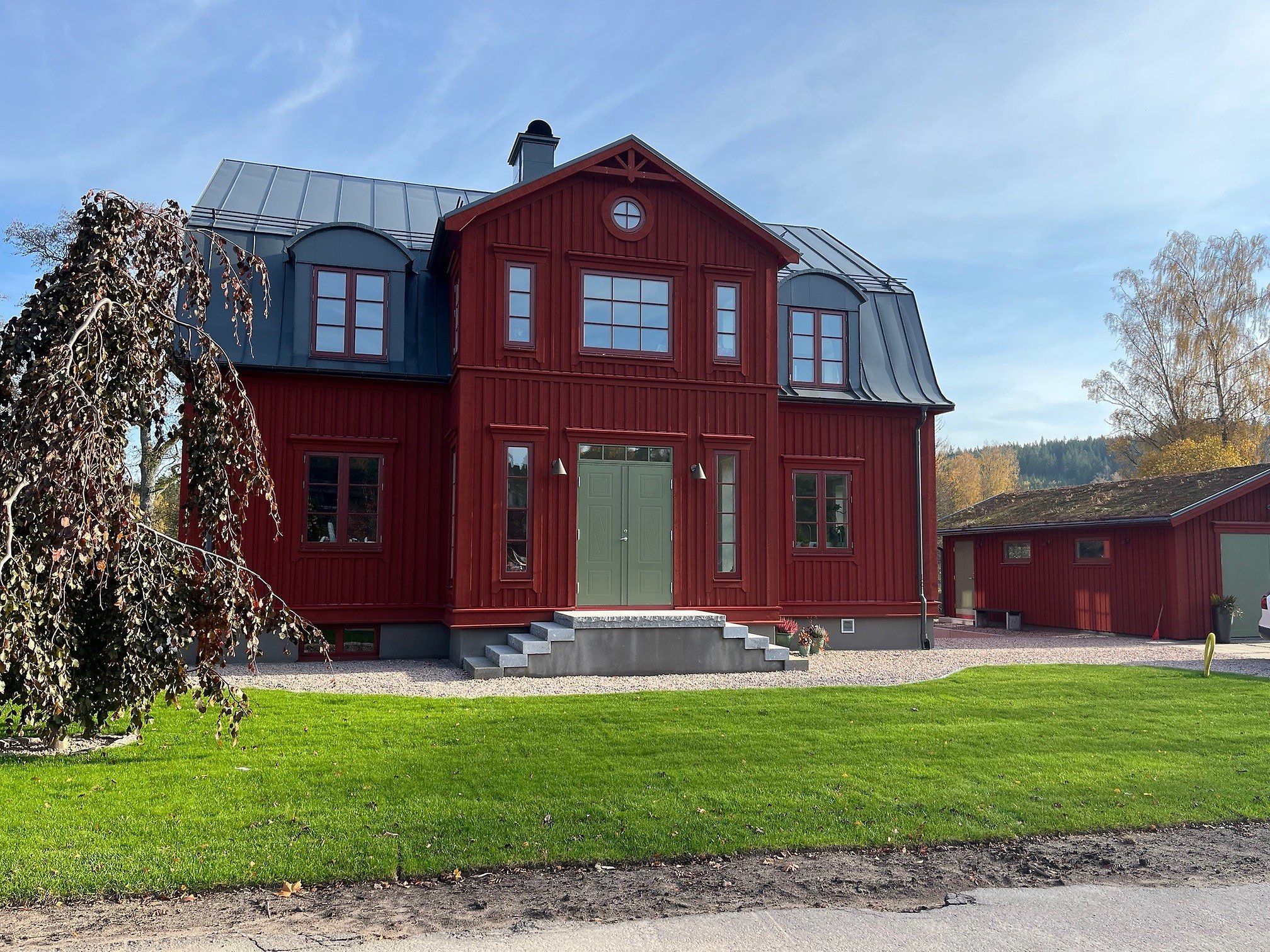 Ett stort rött hus sett framifrån med en trappa upp till den gröna dörren.