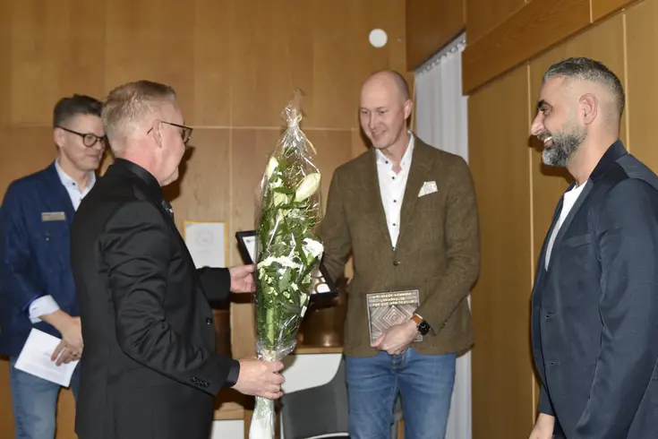 En man delar ut en blombukett till två andra män. I bakgrunden syns ytterligare en man.