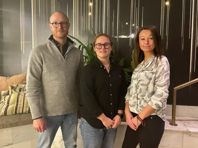 En man och två kvinnor står bredvid varandra och tittar leende in i kameran.