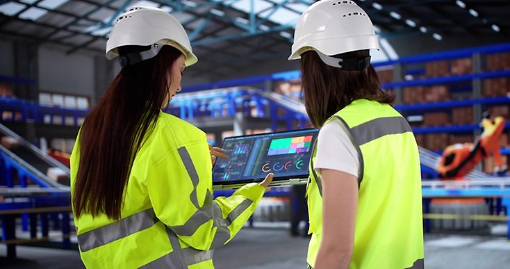 Två personer i en industri tittar på en lästplatta med grafer.