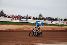 Speedwayförare från Lejonen åker ärevarv med en lejonenflagga i handen. 