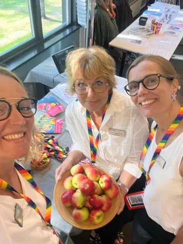 Bild på tre kvinnor som håller i en skål med äpplen.