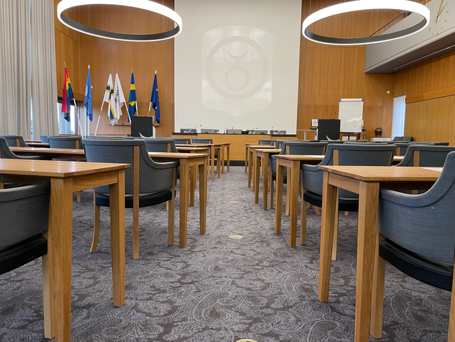 Flera uppradade stolar. Längst bort i rummet finns ett podie med en stor vit duk bakom.