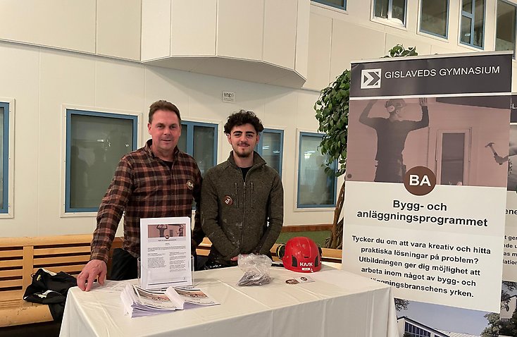 Två män står bakom ett bord och tittar in i kameran.