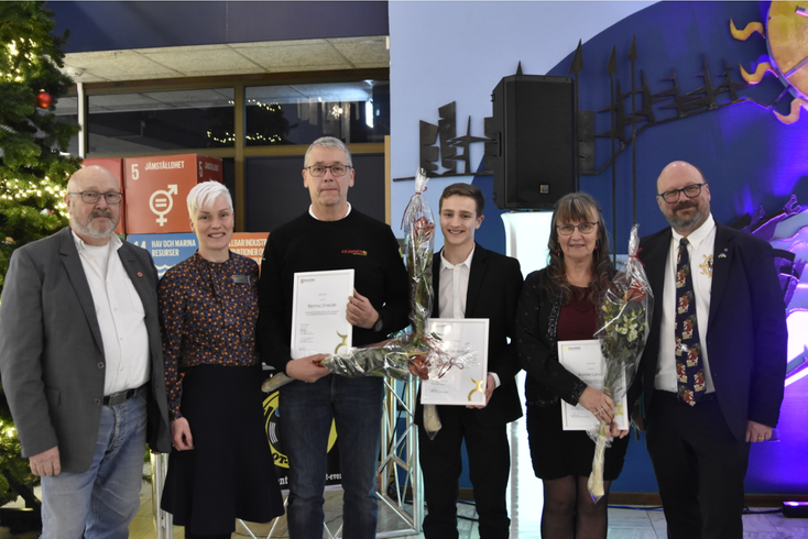 Sex personer står bredvid varandra. Tre av dem håller i varsin blomma och diplom.