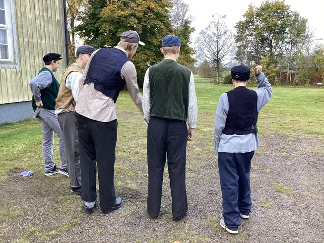 Foto på en grupp pojkar i tidsenliga kläder, de spelar kula.