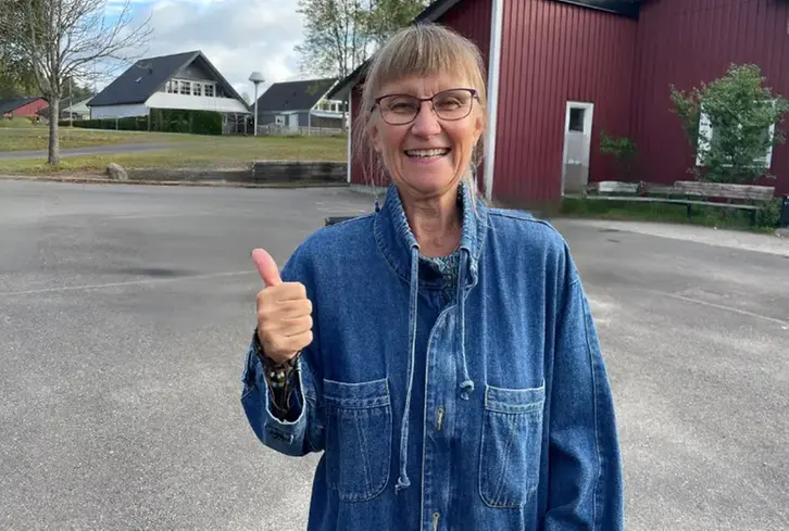 En kvinna som står framför en skola och gör tummen upp.