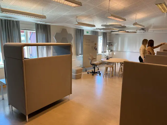 Foto på ett rum fyllt med olika fåtöljer, bås, bord med mera.