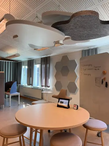 Foto på en del av ett rum, man ser ett bord, stolar och moln som hänger i taket.