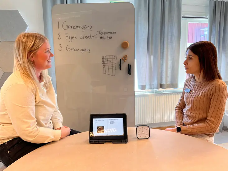 Foto på två kvinnor som sitter vid ett bord och pratar.