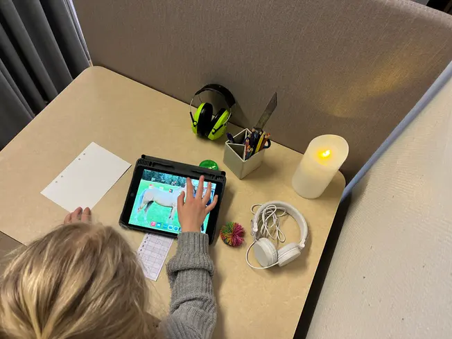 Foto på ett barn ovanifrån, hen sitter vid ett bord där det ligger gröna hörlurar.