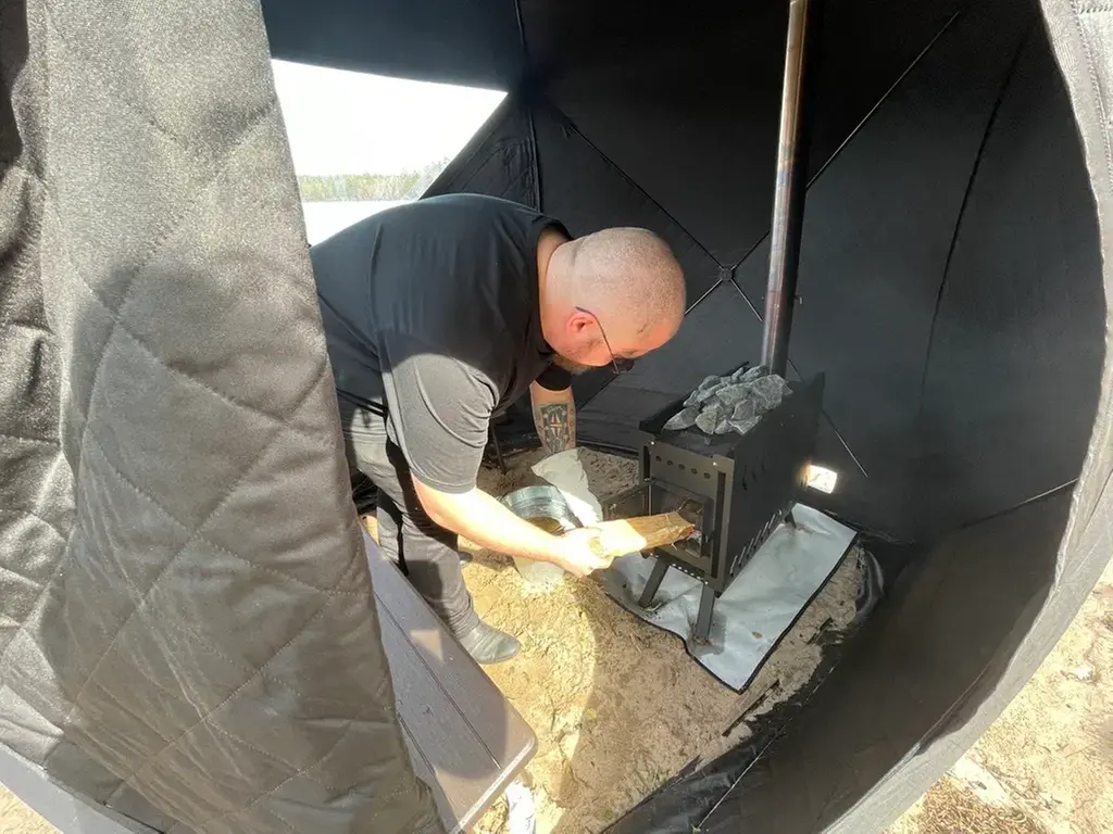 En man lägger in ved i bastun.