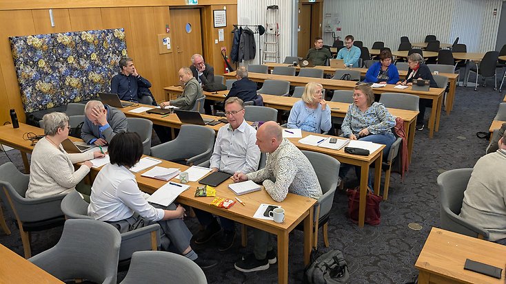 politiker och tjänstemän sitter i smågrupper i kommunfullmäktigesalen.
