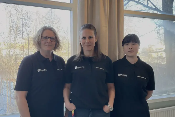 Tre kvinnor står bredvid varandra framför ett fönster och tittar in i kameran. Alla har svarta pikétröjor på sig.