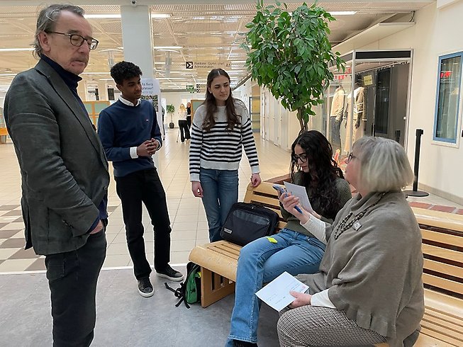 Tre ungdomar vid en bänk samtalar med två äldre personer.