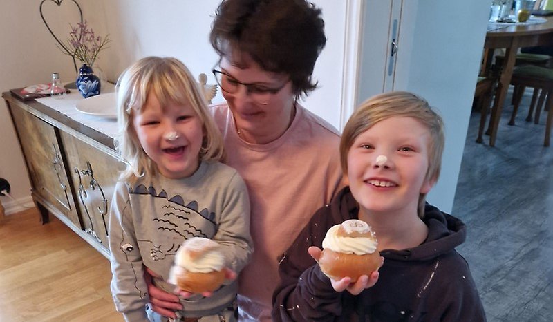 En kvinna med två barn framför sig som håller i varsin semla.