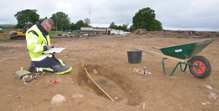 en man som sitter på knä och tittar på ett papper vid en utgrävning