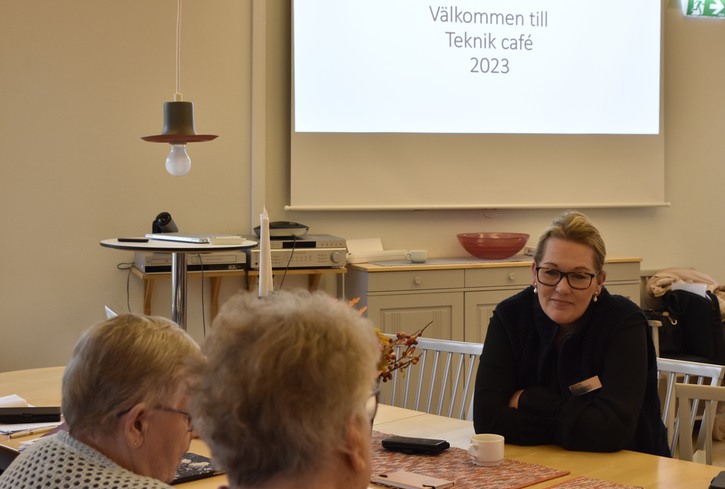 Tre kvinnor sitter vid ett bord. Två av dem sitter med ryggen mot kameran och en med ansiktet mot kameran.