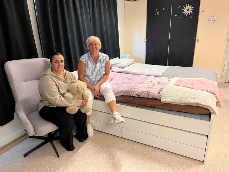 Foto på två kvinnor framföre en dubbelsäng.