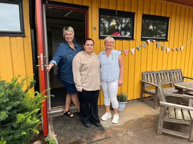 Foto på tre kvinnor som står i dörren till en gul byggnad.